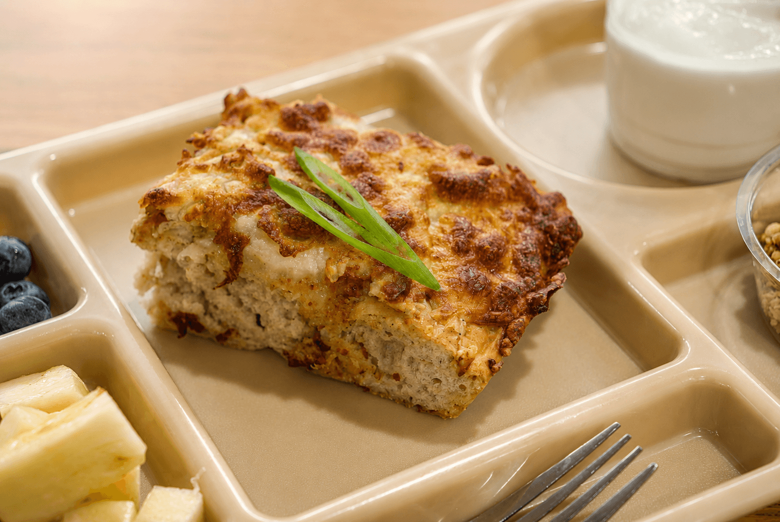A slice of breakfast pizza with a browned cheese top and sliced green onion.