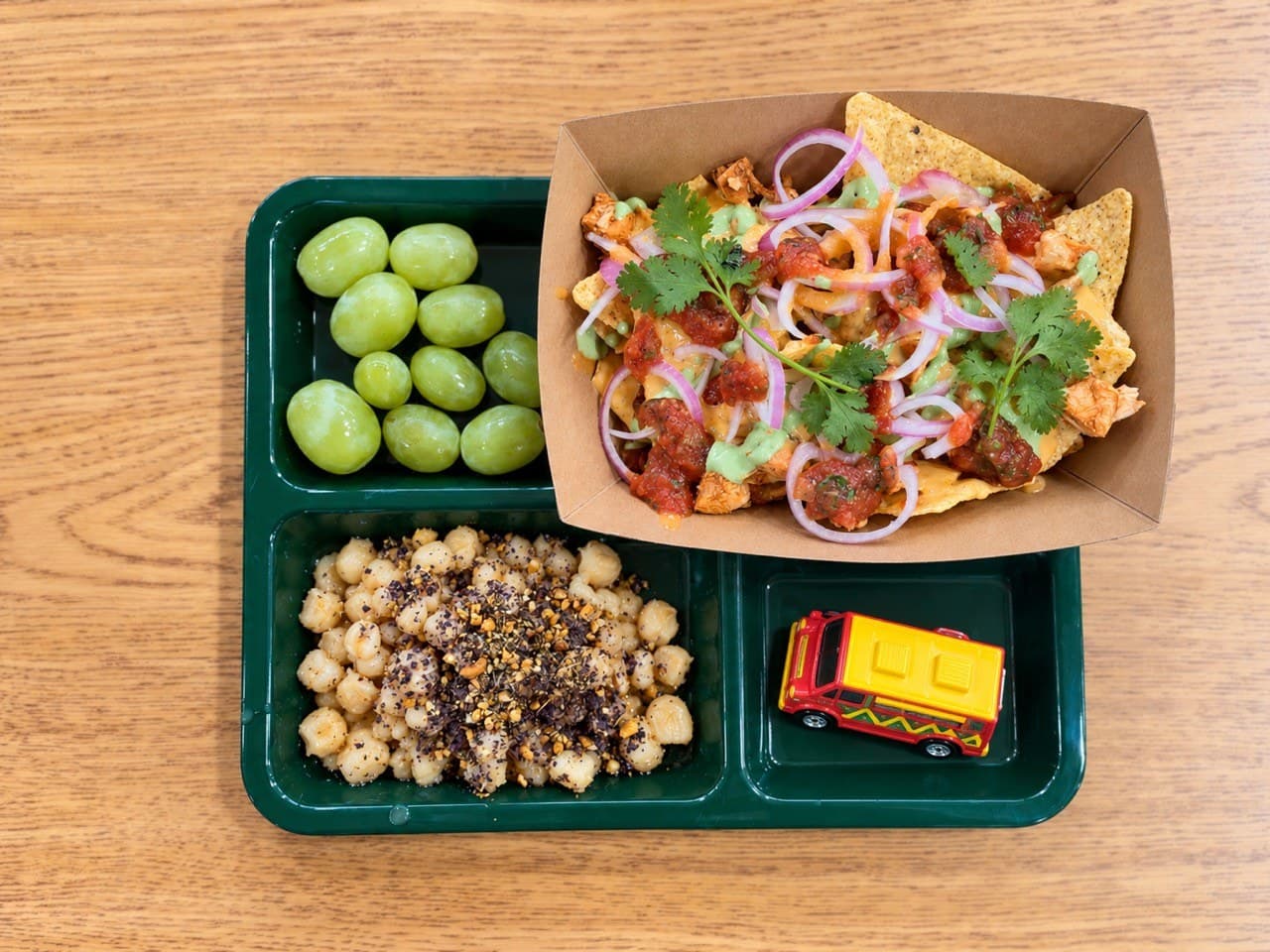 Chopped chicken nachos with queso, salsa, pickled onions and cilantro, beside hominy with a blue corn topping and green grapes.