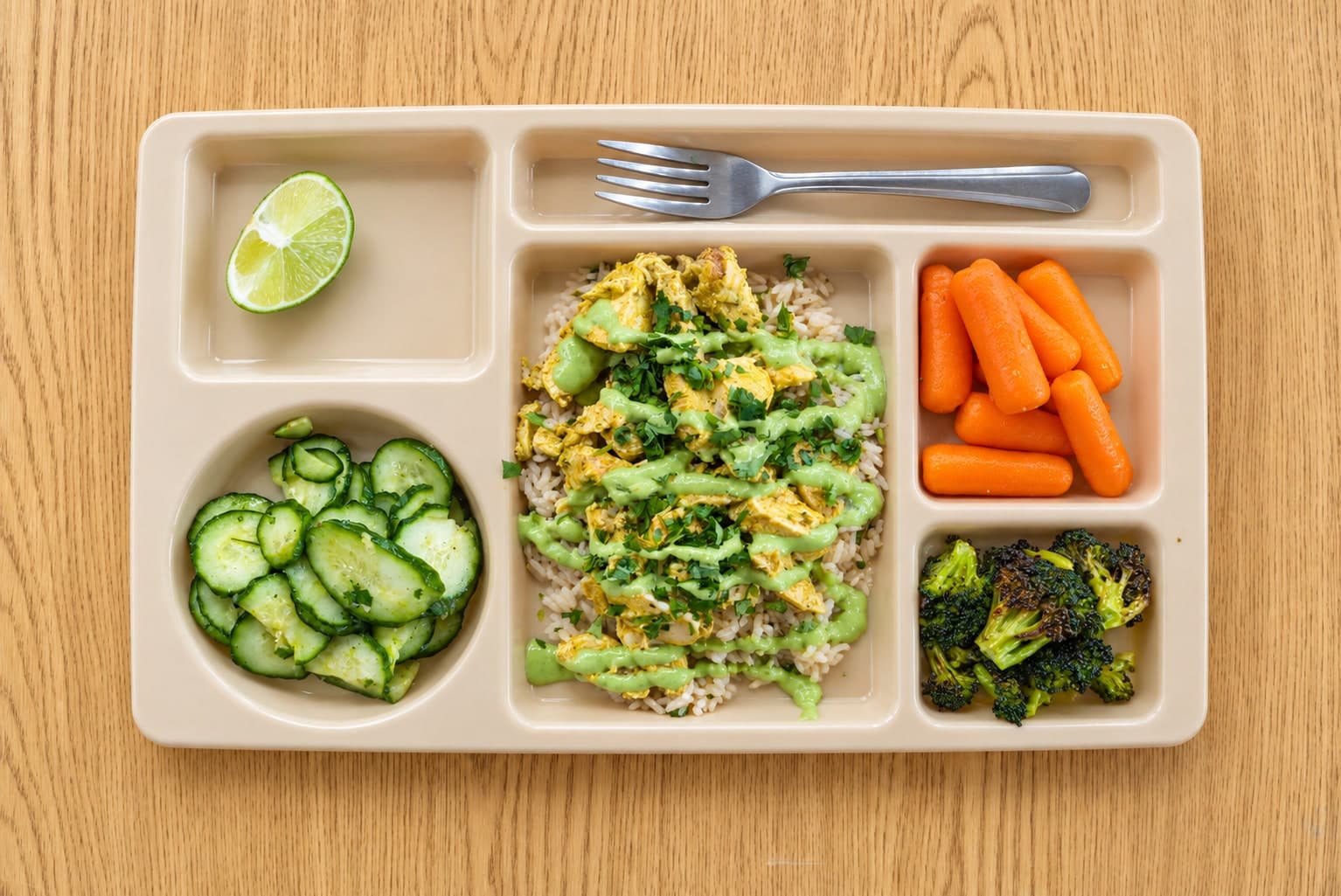 Peruvian chicken and green herb sauce over rice, with cucumbers, carrots, broccoli and lime on a lunch tray.