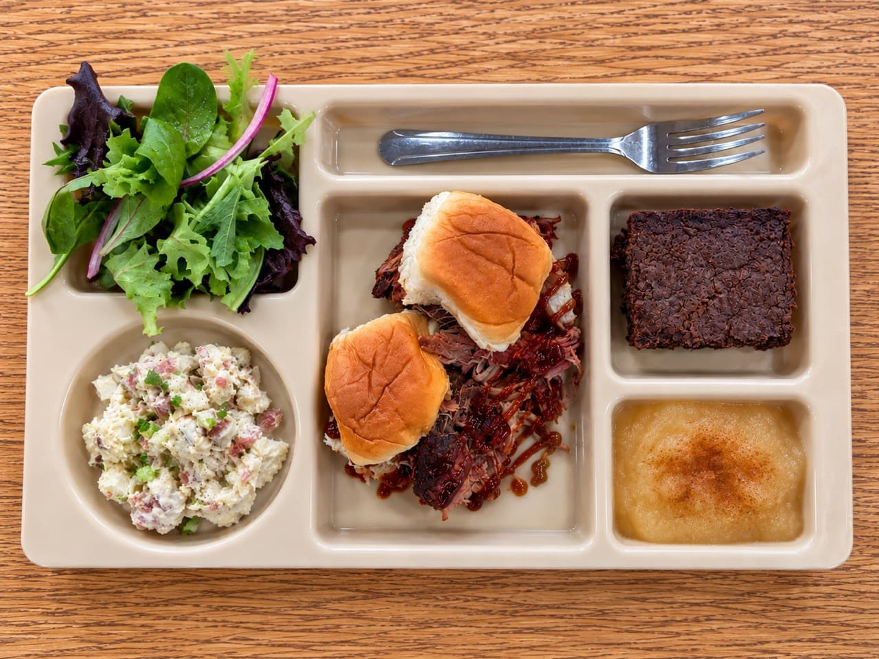 Two pulled pork sliders on Hawaiian rolls with barbecue sauce, potato salad, a fudgy brownie, applesauce and green salad.