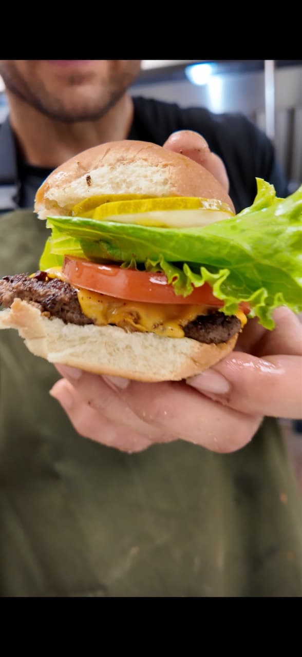 An adult holding a Wagyu smash burger with melted cheese, lettuce, tomato, onion and pickles.